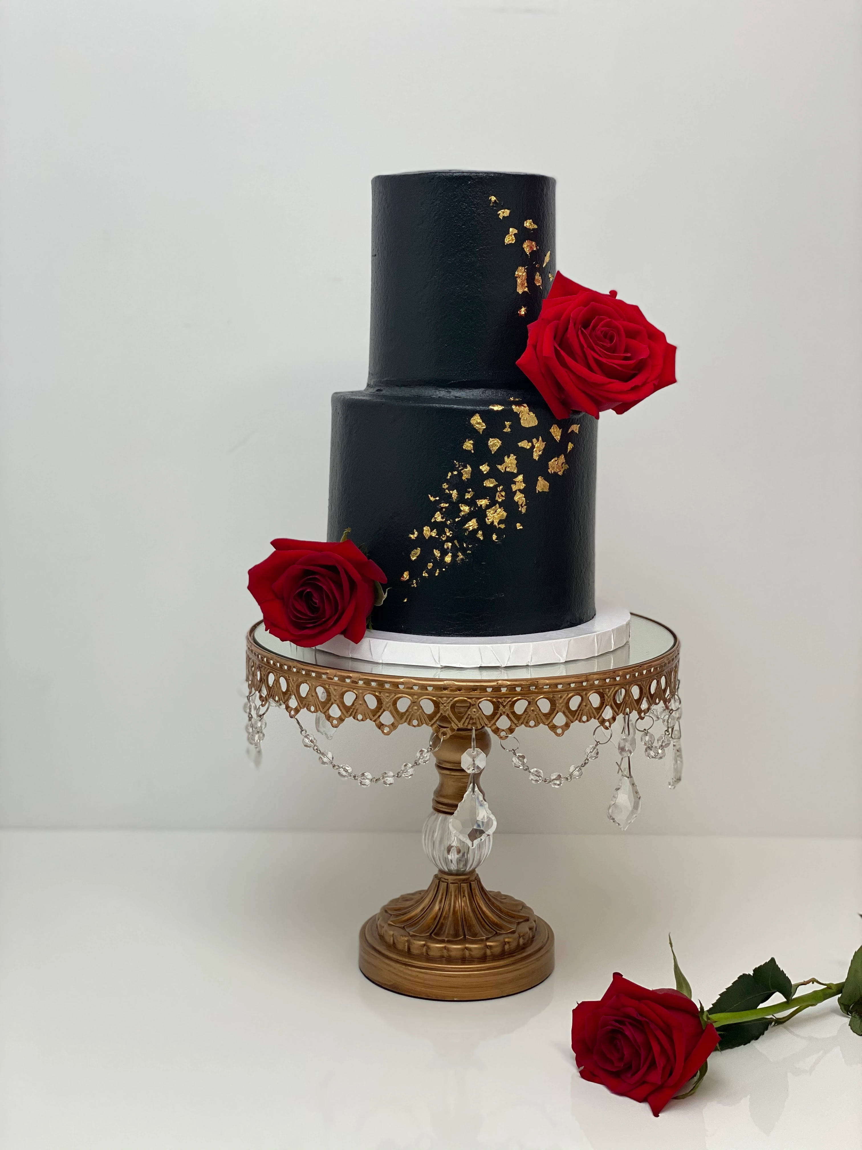 Black cake with 2 roses on a gold cake stand