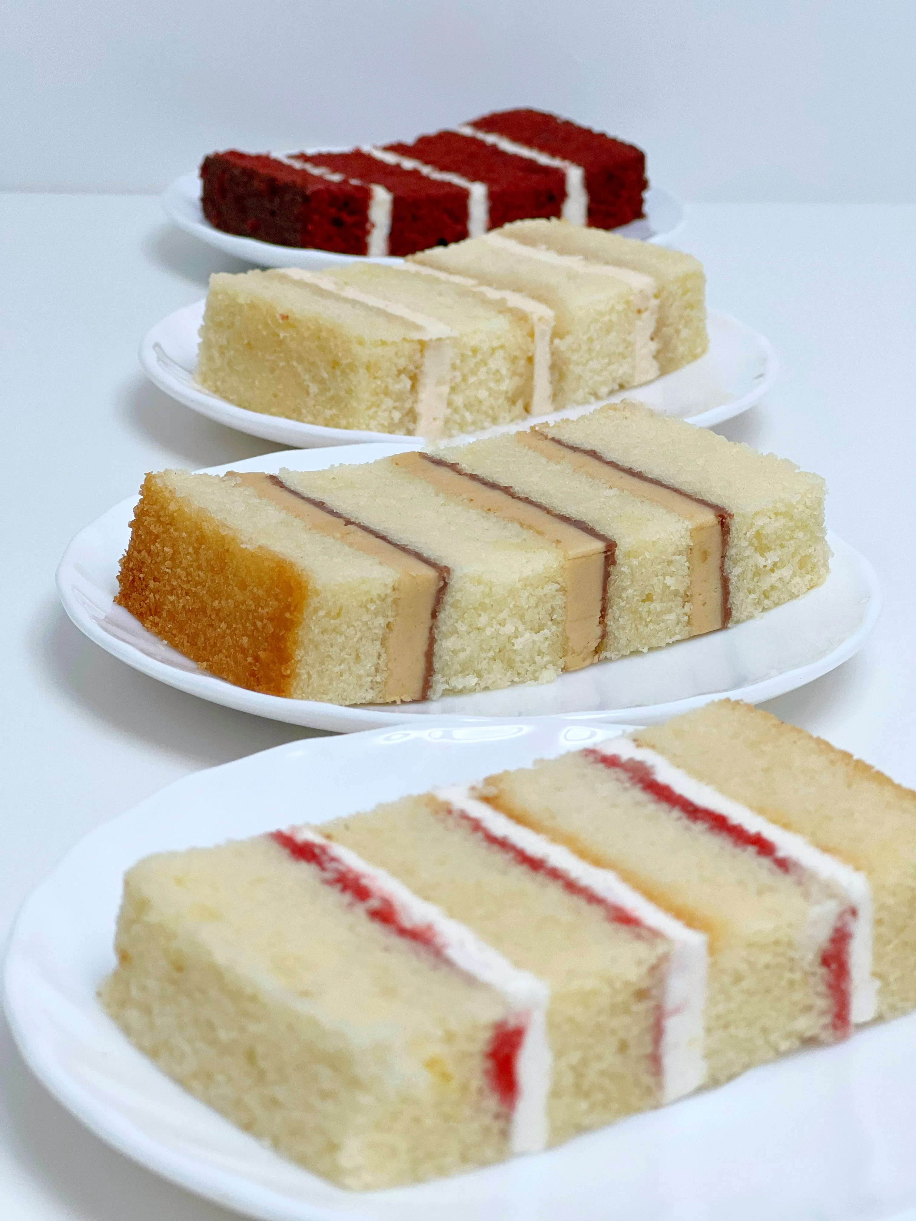 Four individual slices of different flavoured cake in a vertical line